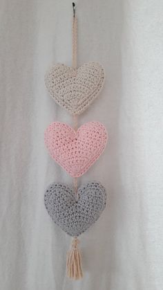 three crocheted hearts hanging from a hook on a white wall with a tassel