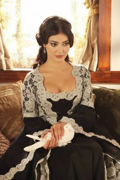 a woman sitting on top of a couch wearing a black dress with white lace trims