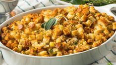 a casserole dish filled with stuffing and garnished with fresh sage leaves