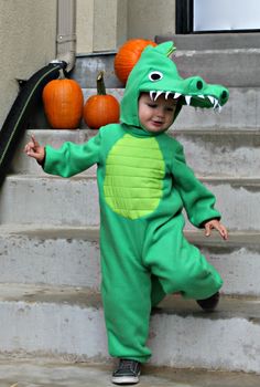 a little boy in a green alligator costume standing on steps with pumpkins behind him