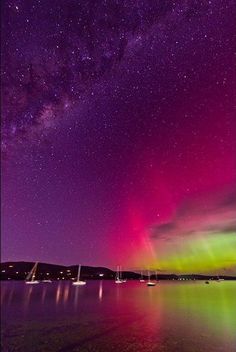 the night sky is filled with stars and colorful lights as boats are in the water