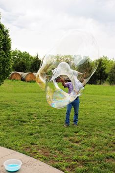 a man is blowing bubbles on the grass in front of a blue bowl and trees