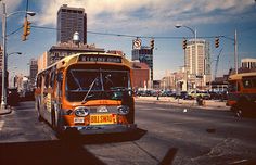 an orange bus is driving down the street in front of some tall buildings and traffic lights