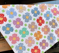 a colorful quilt hanging from the side of a wooden structure with flowers on it and an old truck in the background