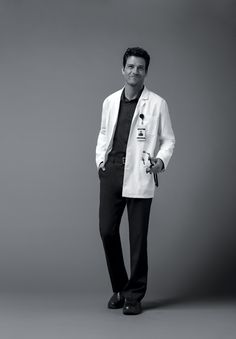 a male in a white lab coat and black pants is posing for a photo with his hands in his pockets