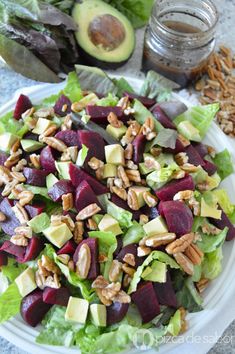 a salad with beets, avocado and pecans on top is sitting on a white plate