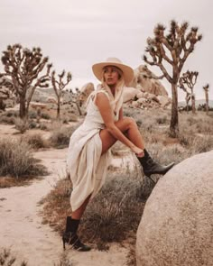 a woman sitting on top of a large rock in the middle of a desert area