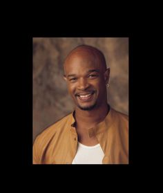 a smiling man in a tan jacket and white t - shirt