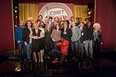 a group of people standing on top of a stage posing for a photo in front of a red curtain