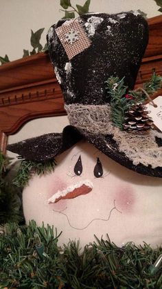 a close up of a snowman with a hat on it's head and evergreen branches