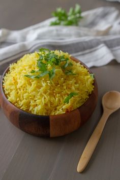 a wooden bowl filled with yellow rice next to a spoon and napkin on a table