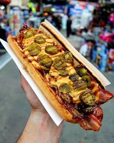 a hand holding a hot dog with bacon and jalapeno peppers on it