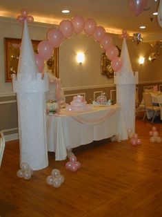 a table set up for a princess party with pink balloons and castle shaped cake on it