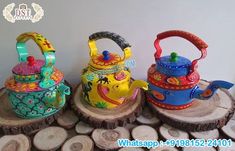 three colorful tea kettles sitting on top of wooden slices