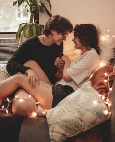 two people sitting on a couch with christmas lights all around them and one person touching the other's cheek