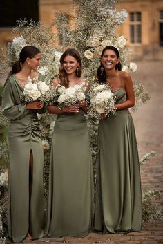 three bridesmaids standing in front of an arch with white flowers and greenery