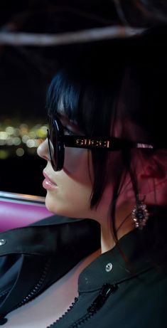 a woman wearing sunglasses sitting in the back seat of a car with city lights behind her