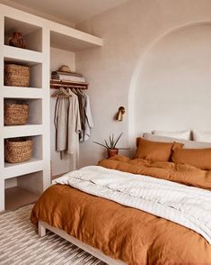 a bed with an orange comforter in a bedroom next to a white wall and shelves