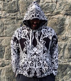 a man standing in front of a stone wall wearing a black and white hoodie