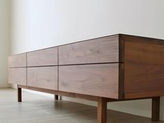 a wooden dresser sitting on top of a hard wood floor next to a white wall