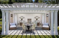 an outdoor dining area with white furniture and pergolated roofing, surrounded by lush green grass