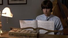 a young man sitting at a desk with music sheets in front of him and a lamp next to him