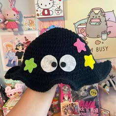 a hand holding up a black hat with eyes and stars on it in front of many other toys