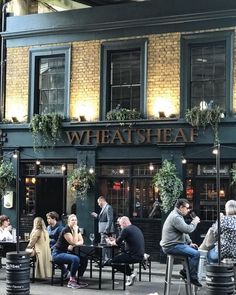 people sitting at tables in front of a building with windows and plants growing on it