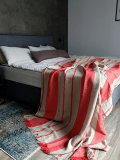 a bed with a red and white blanket sitting on top of it next to a rug