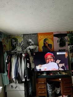 a room with clothes hanging on the wall and a flat screen tv sitting on top of a dresser