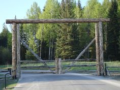 an old wooden gate in the middle of a road surrounded by pine trees and grass