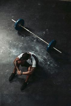 a man sitting on the ground with a barbell in his hand and looking down