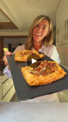 a woman holding up two pizzas on top of a tray in the kitchen,