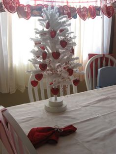 a white christmas tree with red hearts on it in the corner of a dining room