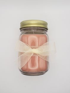 a pink candle in a glass jar with a bow