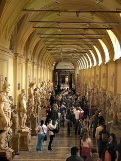 many people are walking around in an old building with statues on the walls and ceilings