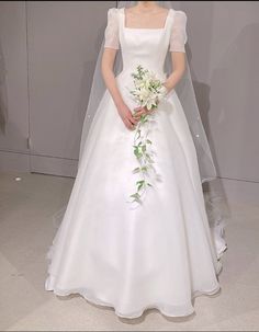 a woman in a white wedding dress holding a bouquet and standing next to a wall