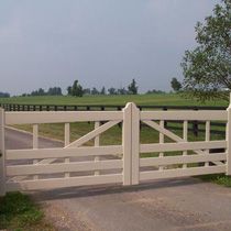 a white gate is open on the side of a road with a tree in the background