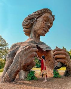 a woman standing in front of a large wooden statue