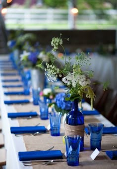 the table is set with blue and white flowers in vases, napkins, and place settings