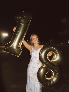 a woman in a white dress holding up an air filled number 8 balloon at night