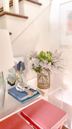 a glass table topped with a vase filled with flowers next to a stair case and lamp