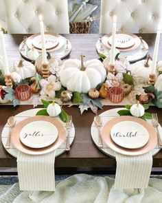 the table is set with white pumpkins, greenery and gold place settings for dinner