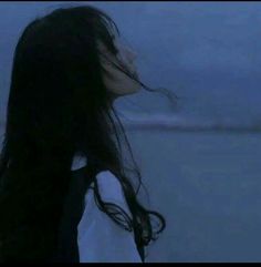 a woman with long black hair standing in front of the ocean at night looking into the distance