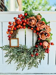 a wreath with red berries and greenery is hung on a white picketle wall