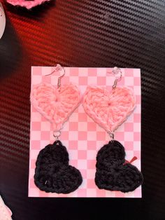 two crocheted heart shaped earrings sitting on top of a pink and black checkered table