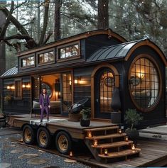 a woman standing on the deck of a tiny house in the middle of a forest