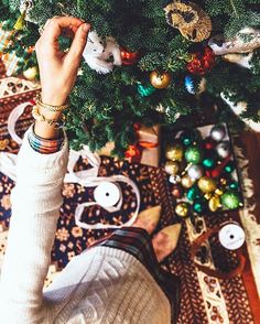 someone holding their hand up in front of a christmas tree that is decorated with ornaments