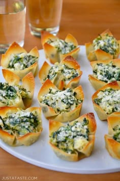 small appetizers with spinach and cheese are on a plate next to a glass of water