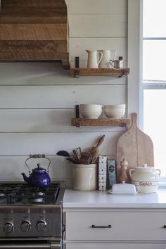 a stove top oven sitting inside of a kitchen next to a wooden shelf filled with pots and pans